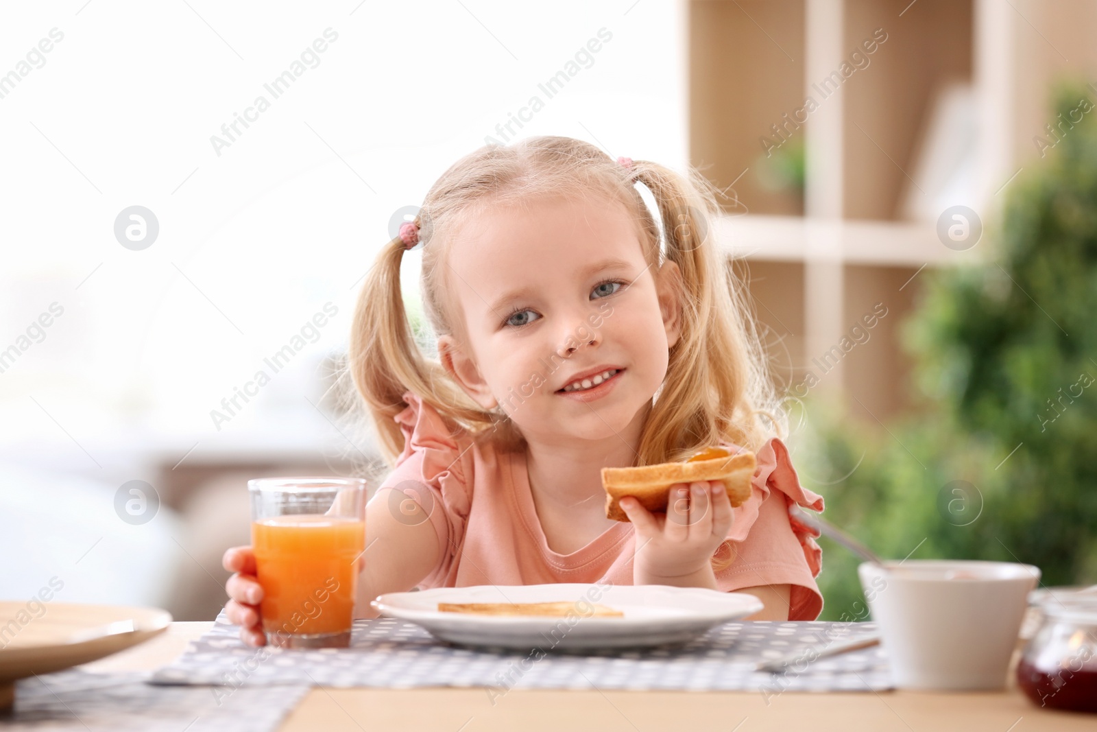 Photo of Cute little girl eating tasty toasted bread with jam at table