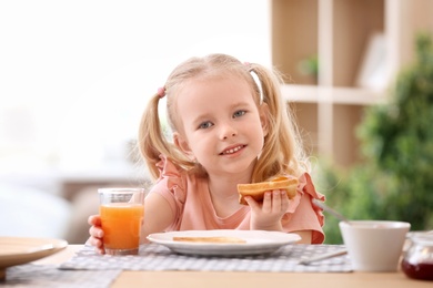 Photo of Cute little girl eating tasty toasted bread with jam at table