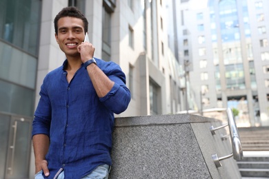 Photo of Handsome young African-American man talking on mobile phone outdoors. Space for text