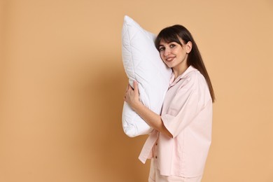 Happy woman wearing pyjama and holding pillow on beige background