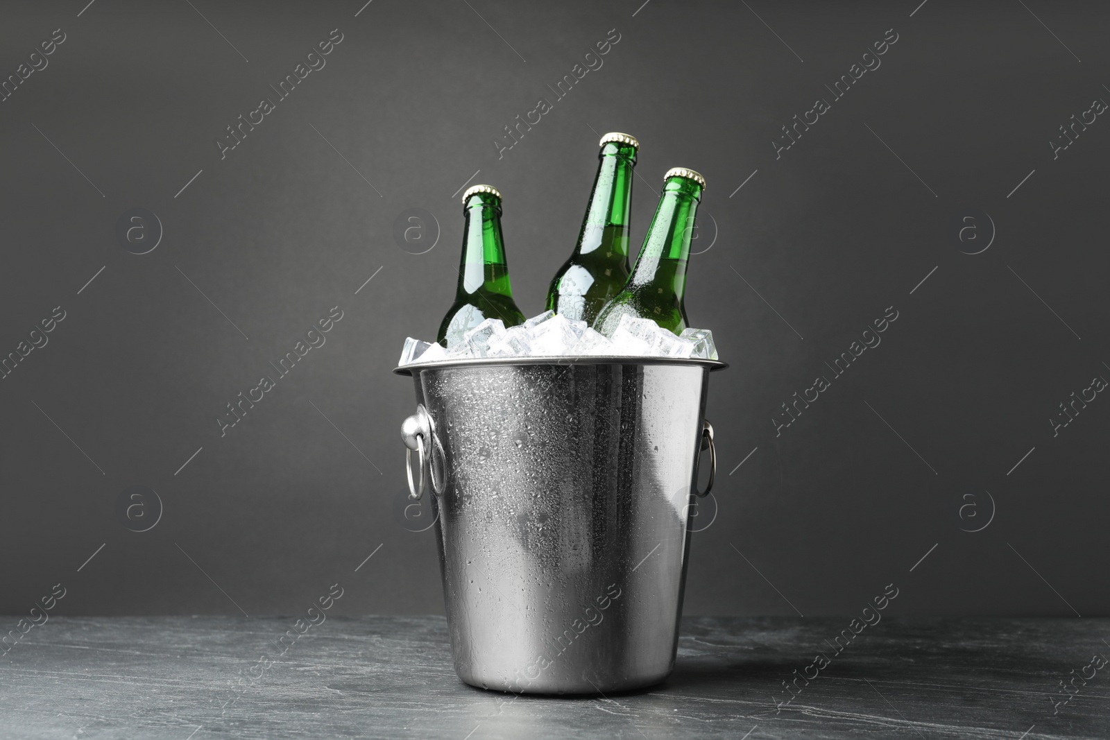 Photo of Metal bucket with bottles of beer and ice cubes on grey background