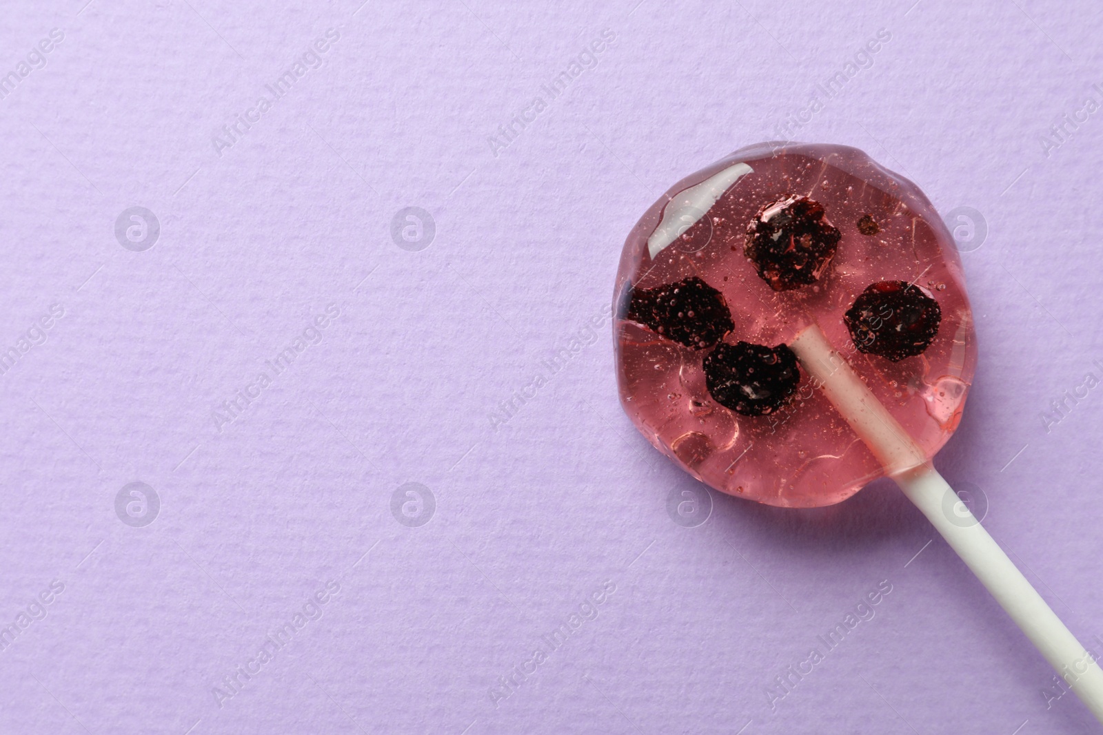 Photo of Sweet colorful lollipop with berries on lilac background, top view. Space for text