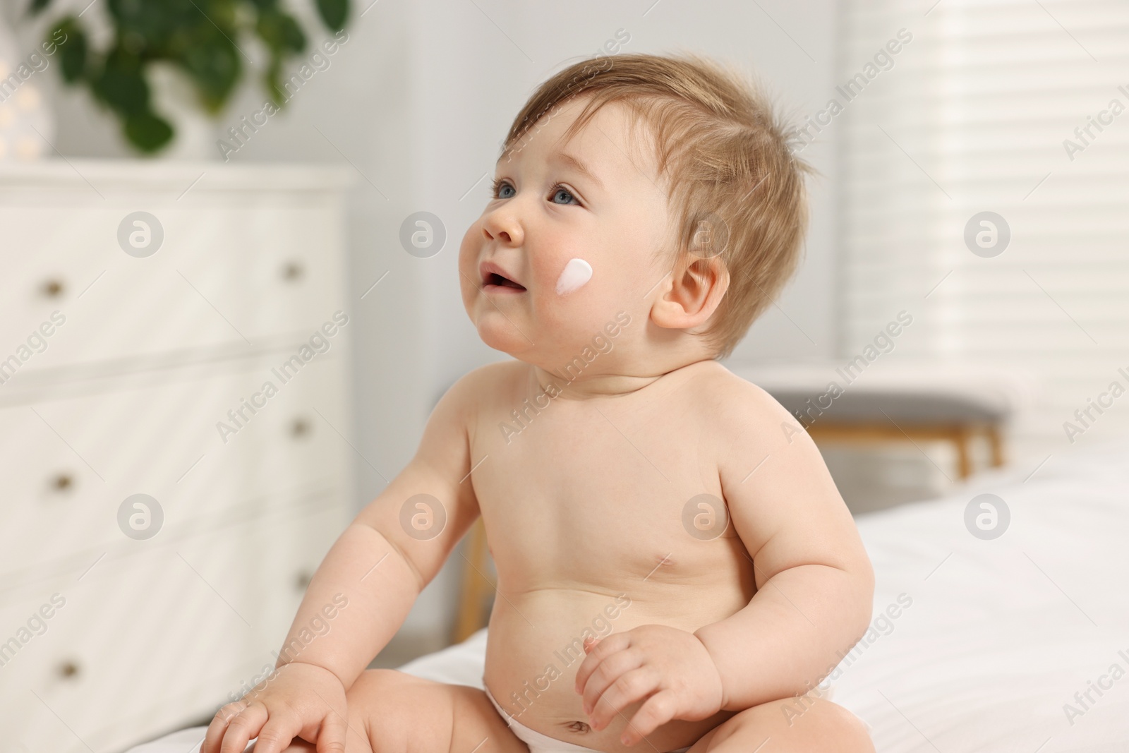 Photo of Cute little baby with moisturizing cream on face at home