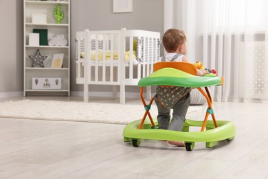 Photo of Cute baby making first steps with toy walker at home, back view. Space for text