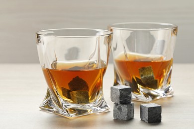 Whiskey stones and drink in glasses on light wooden table, closeup