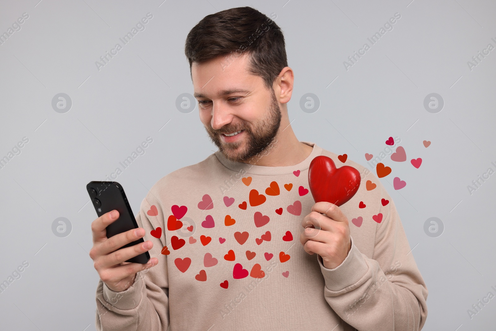 Image of Long distance love. Man video chatting with sweetheart via smartphone on grey background. Hearts flying out of device