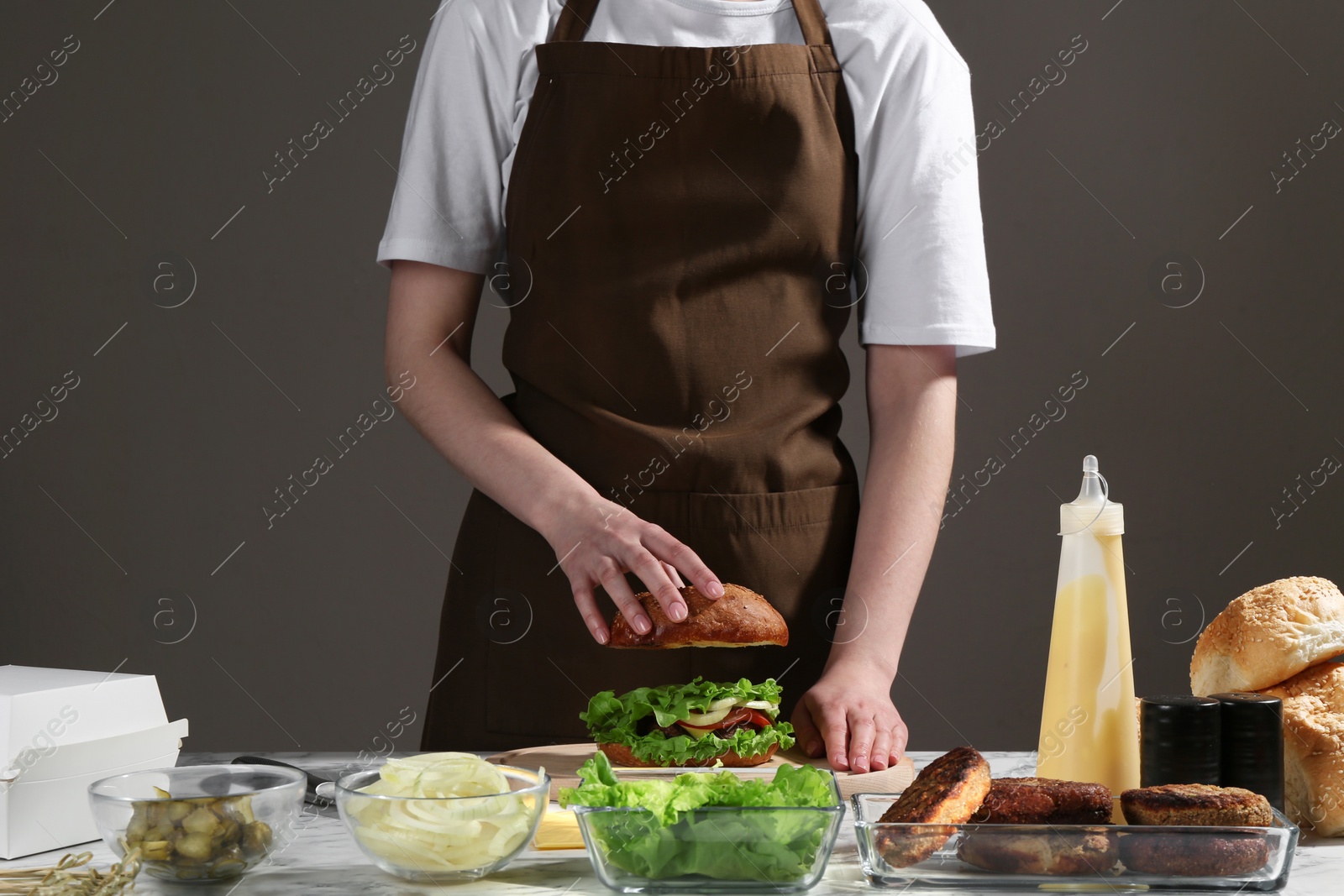 Photo of Woman making delicious vegetarian burger at table, closeup