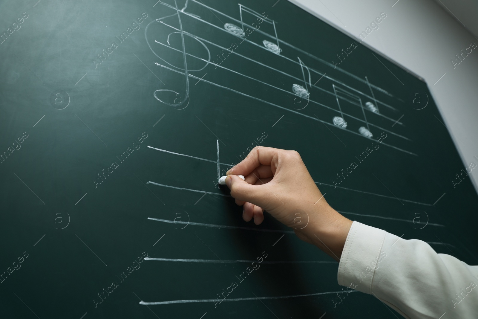 Photo of Teacher writing music notes with chalk on greenboard, closeup