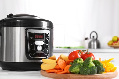 Photo of Modern multi cooker and wooden board with vegetables on white table in kitchen