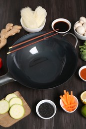 Photo of Empty iron wok and chopsticks surrounded by ingredients on dark grey wooden table