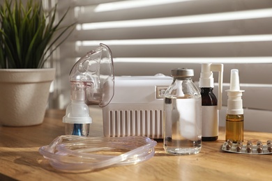 Photo of Modern nebulizer with face mask and medications on wooden table indoors. Inhalation equipment