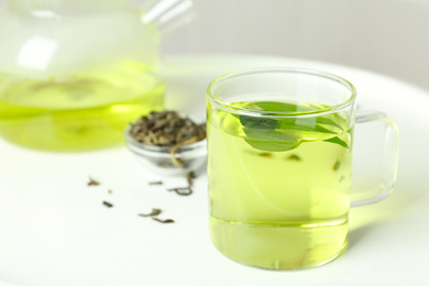 Photo of Cup of aromatic green tea with leaves on white table