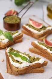 Photo of Tasty bruschetta with cream cheese, pesto sauce and fresh basil on parchment paper, closeup