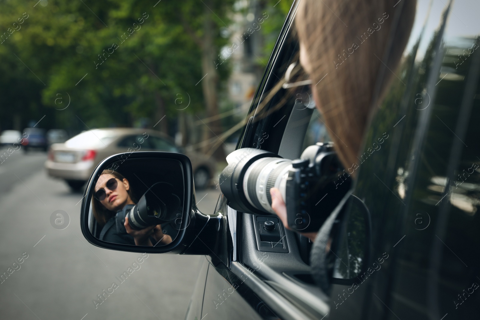 Photo of Private detective with camera spying from auto, view through car side mirror