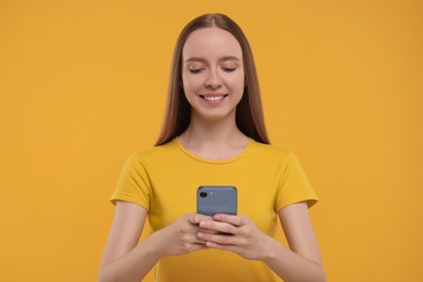 Photo of Happy young woman using smartphone on yellow background