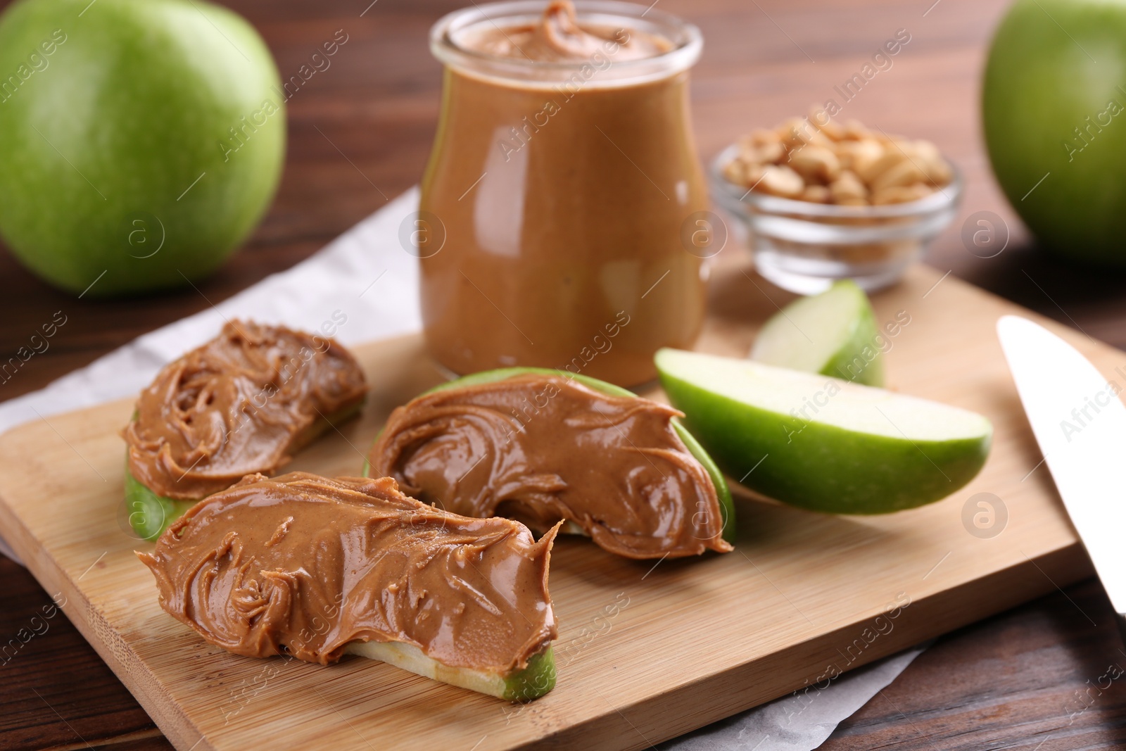 Photo of Slices of fresh green apple with peanut butter on wooden table, closeup