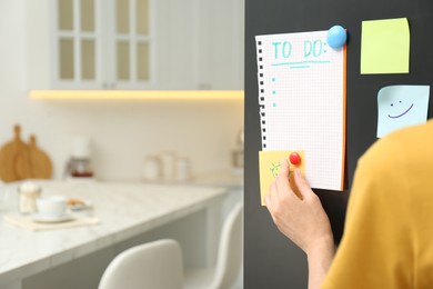 Woman putting blank to do list on refrigerator door in kitchen, closeup. Space for text