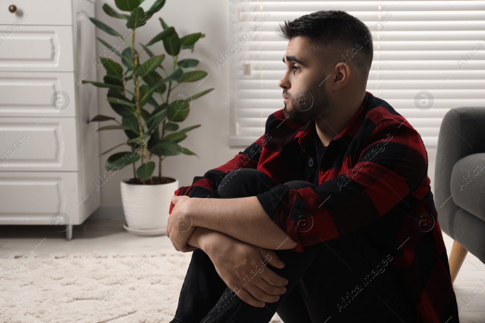 Photo of Sad man sitting on floor at home. Space for text