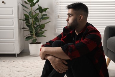 Photo of Sad man sitting on floor at home. Space for text