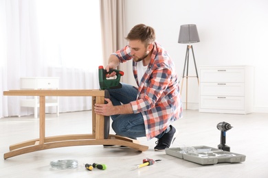 Photo of Young working man repairing chair at home