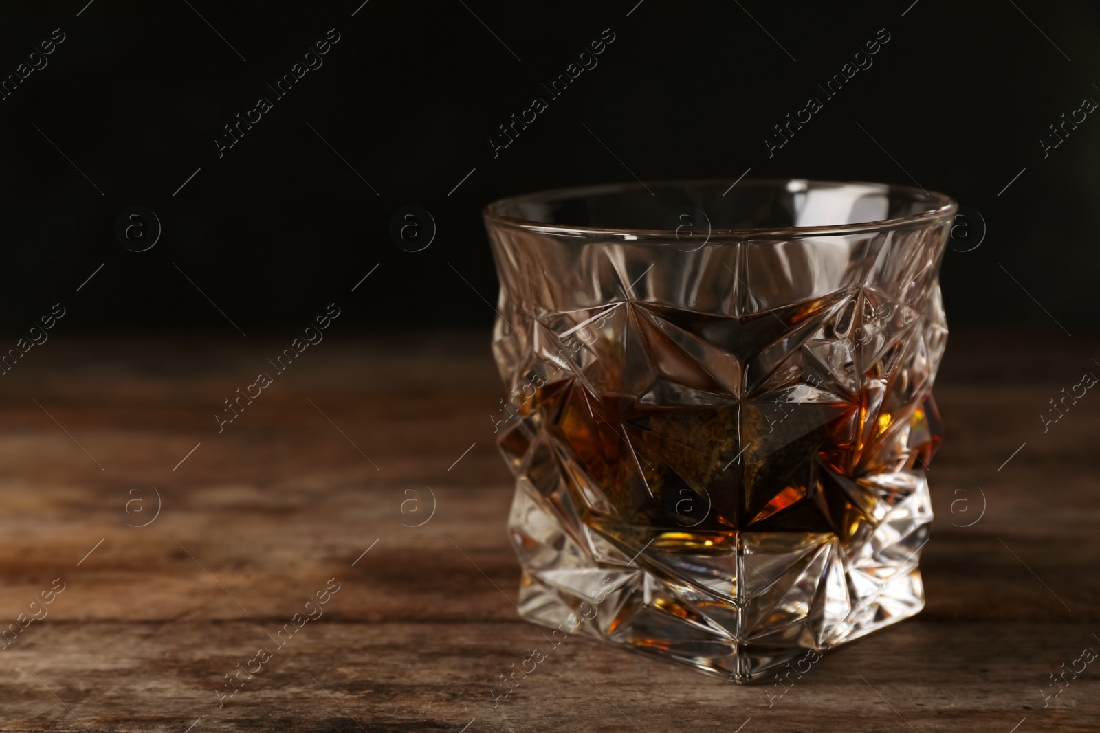 Photo of Golden whiskey in glass with cooling stones on table. Space for text