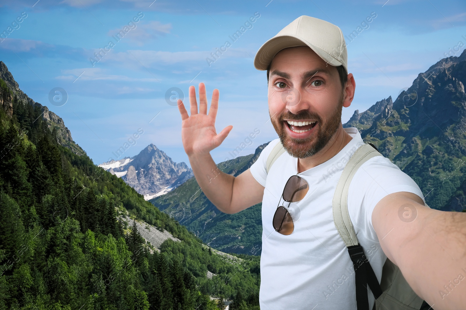 Image of Smiling man waving hand while taking selfie in mountains
