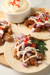 Delicious tacos with vegetables, meat and sauce on white table, closeup