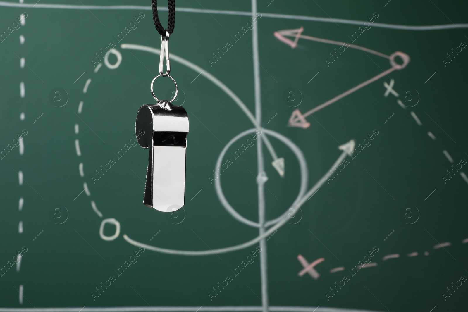 Photo of Referee whistle against green chalkboard with game scheme, closeup. Space for text