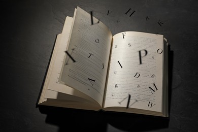 Image of Open book with letters flying out of it on black background