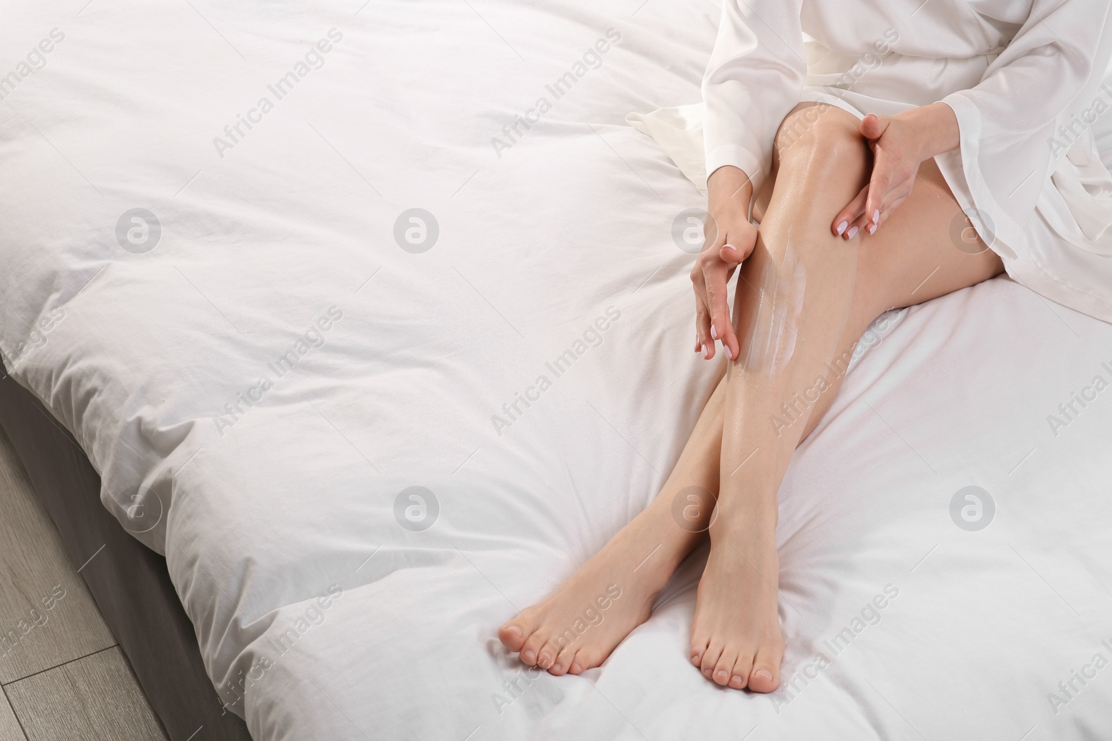 Photo of Woman applying body cream onto her smooth legs on bed, closeup. Space for text