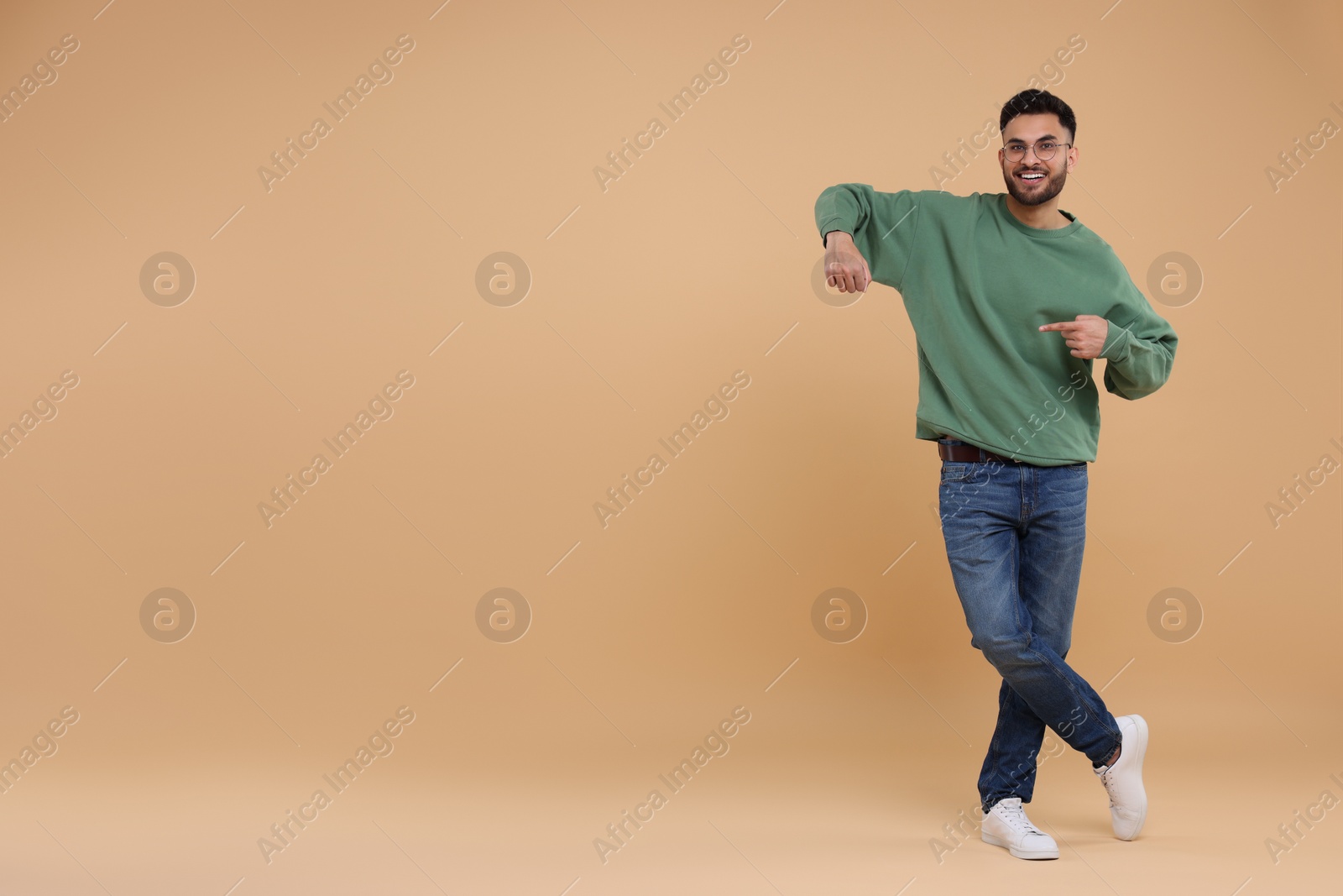 Photo of Happy young man pointing at something on beige background, space for text