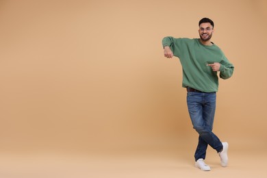 Happy young man pointing at something on beige background, space for text