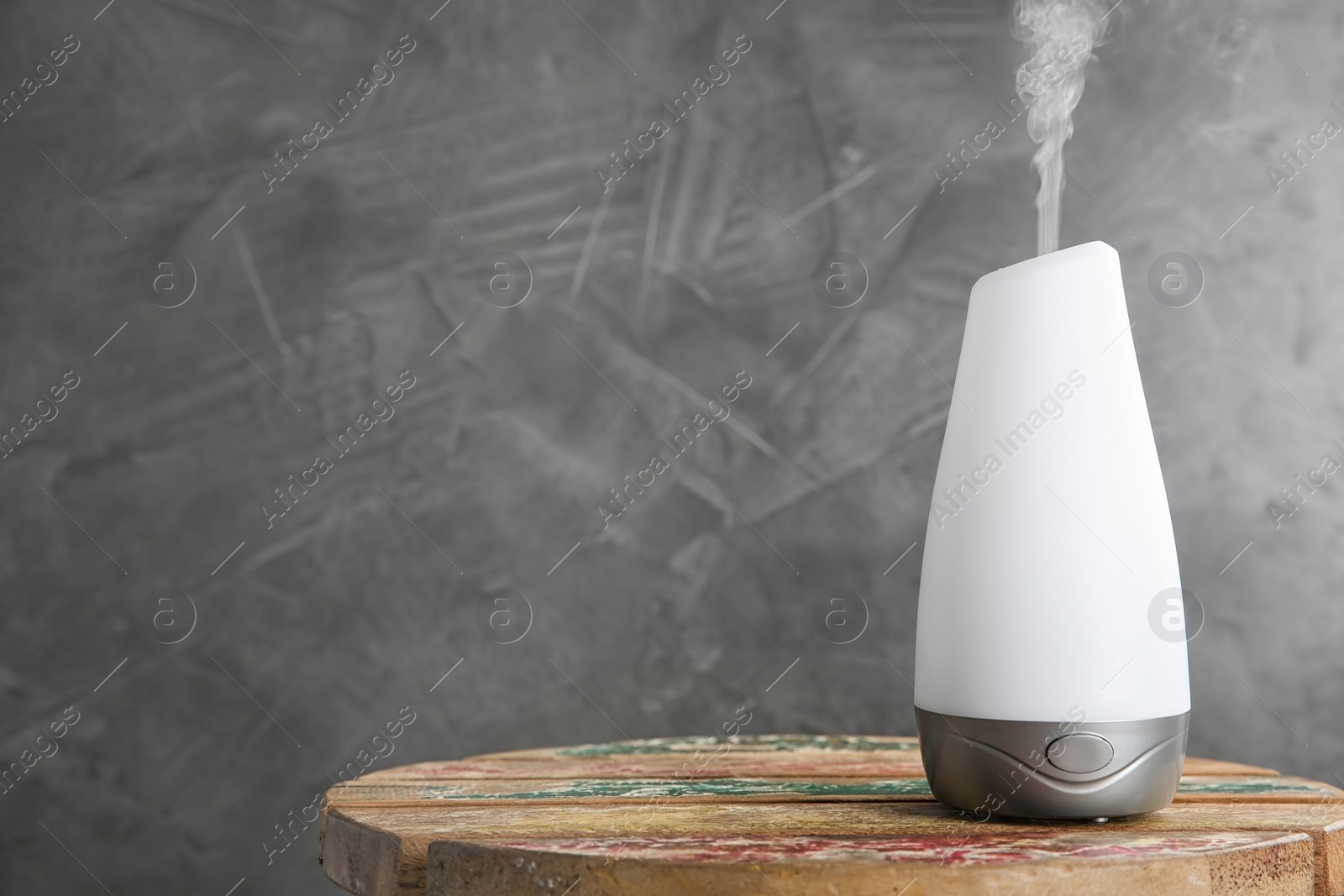 Photo of Modern essential oil diffuser on wooden table against dark grey background. Space for text