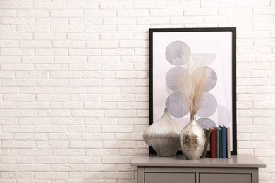 Photo of Grey chest of drawers with decor and books near white brick wall space for text. Interior design