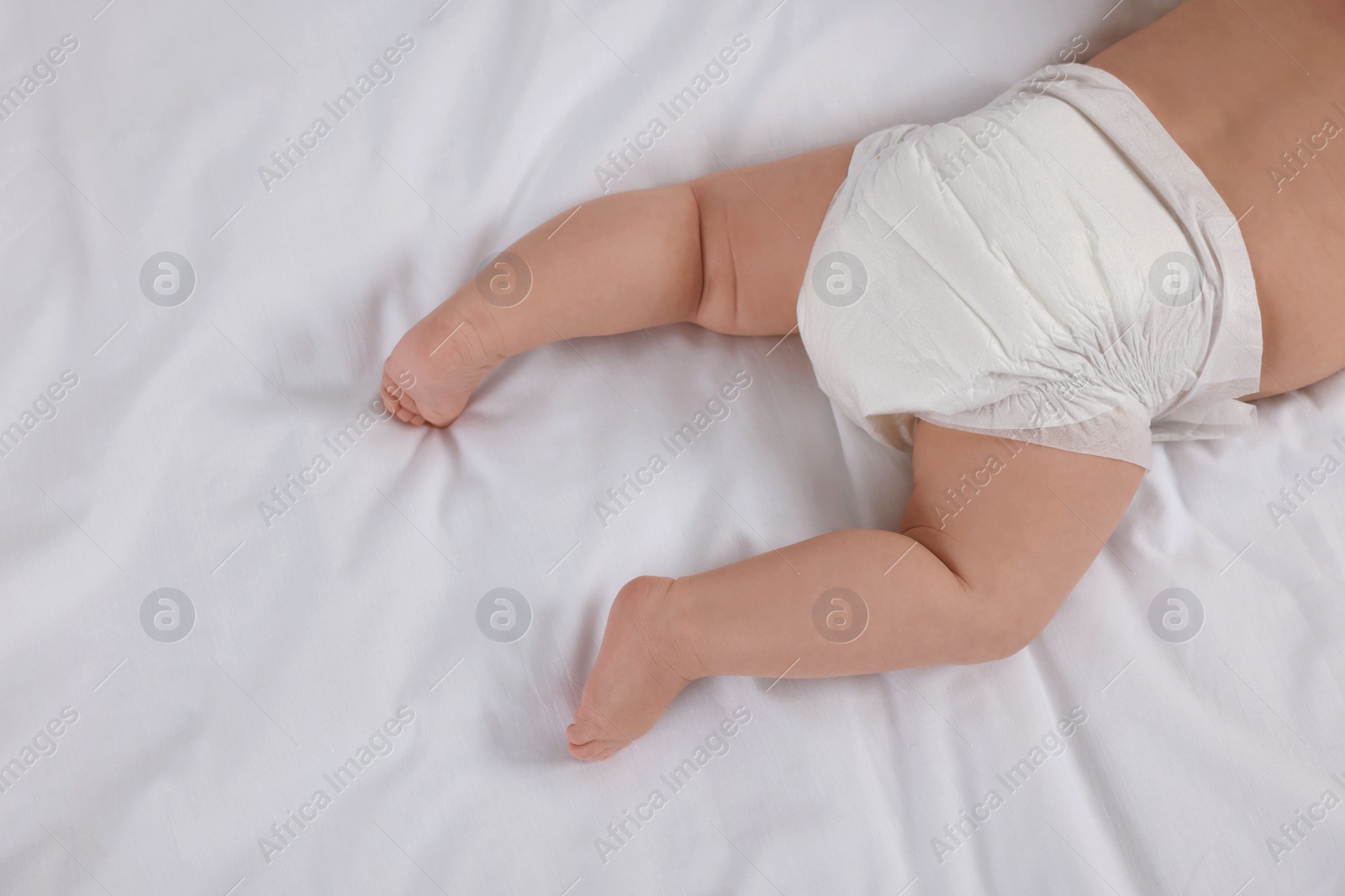 Photo of Little baby in diaper lying on bed, top view