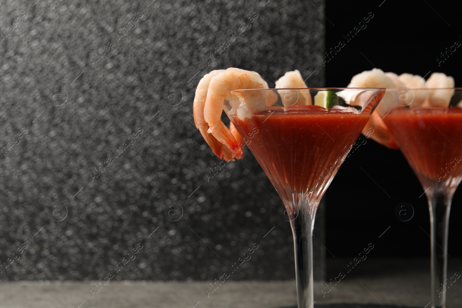 Photo of Tasty shrimp cocktail with sauce and lime in glasses on grey table, space for text