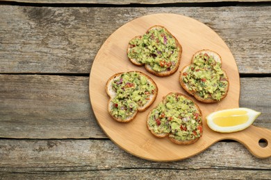 Photo of Slices of bread with tasty guacamole and lemon on wooden table, top view. Space for text