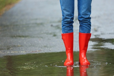 Photo of Woman with red rubber boots in puddle, closeup. Rainy weather