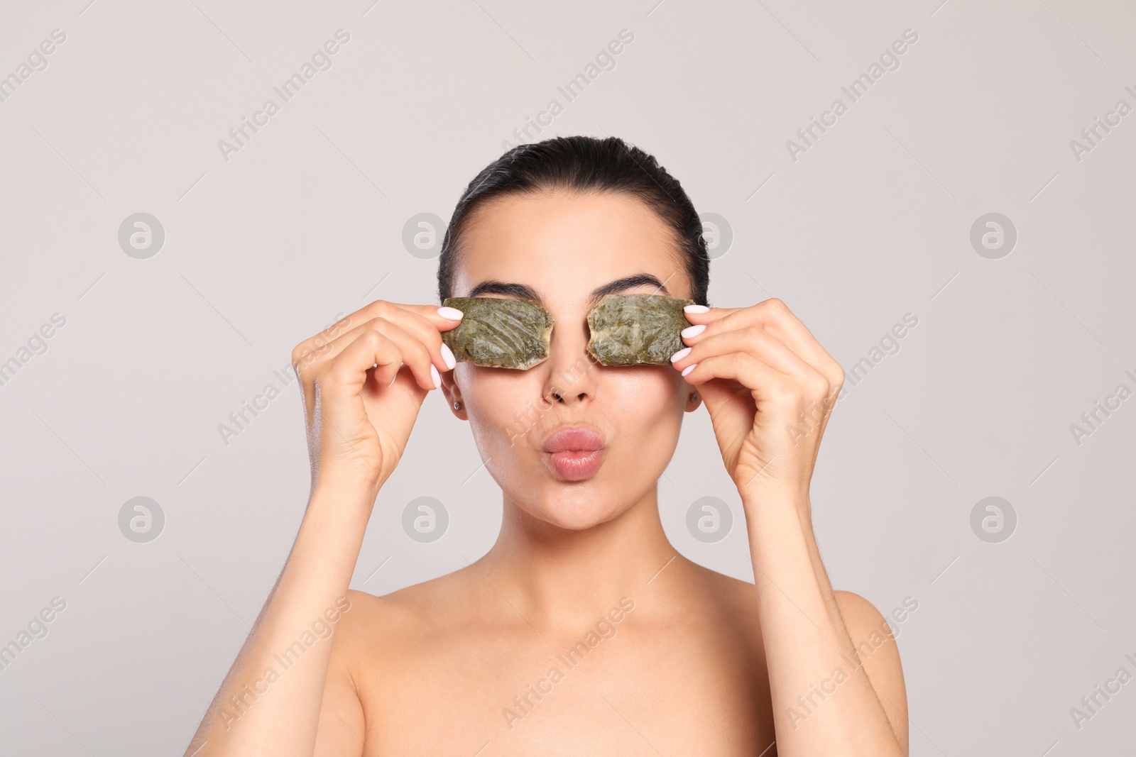 Photo of Beautiful young woman putting green tea bags on eyes against light grey background