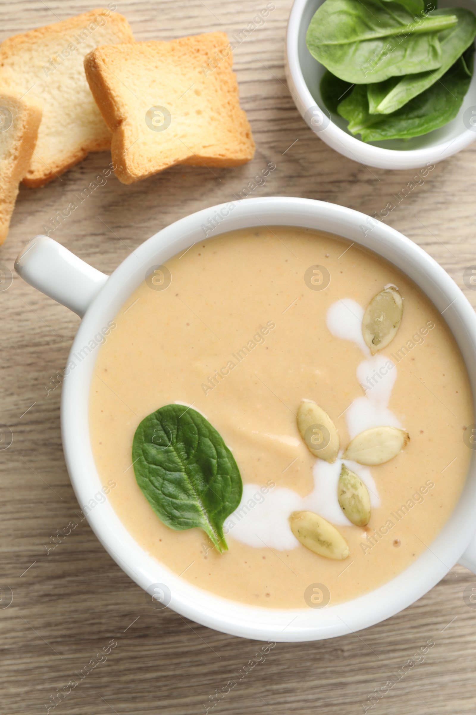 Photo of Healthy cream soup high in vegetable fats, bread and spinach on wooden table, flat lay