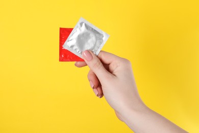 Photo of Woman holding condoms on yellow background, closeup