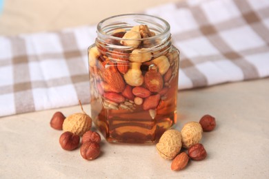 Jar with different nuts and honey on beige table