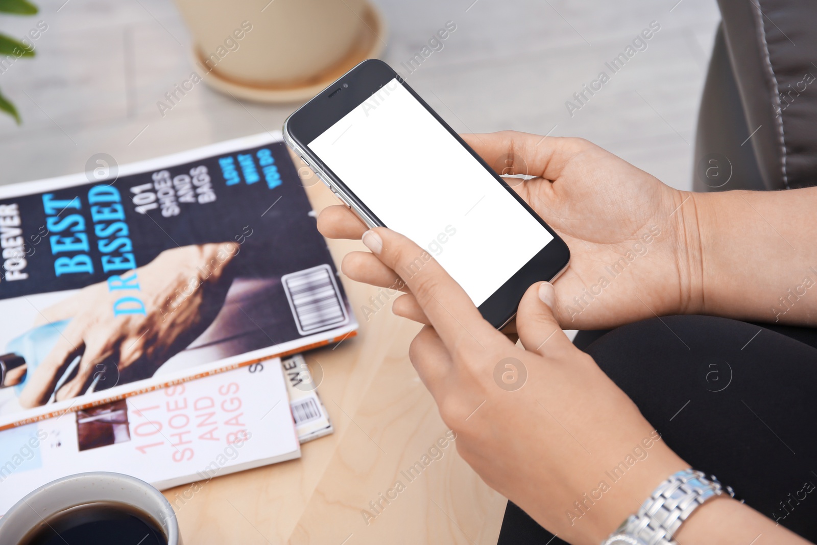 Photo of Young woman holding mobile phone with blank screen in hands indoors