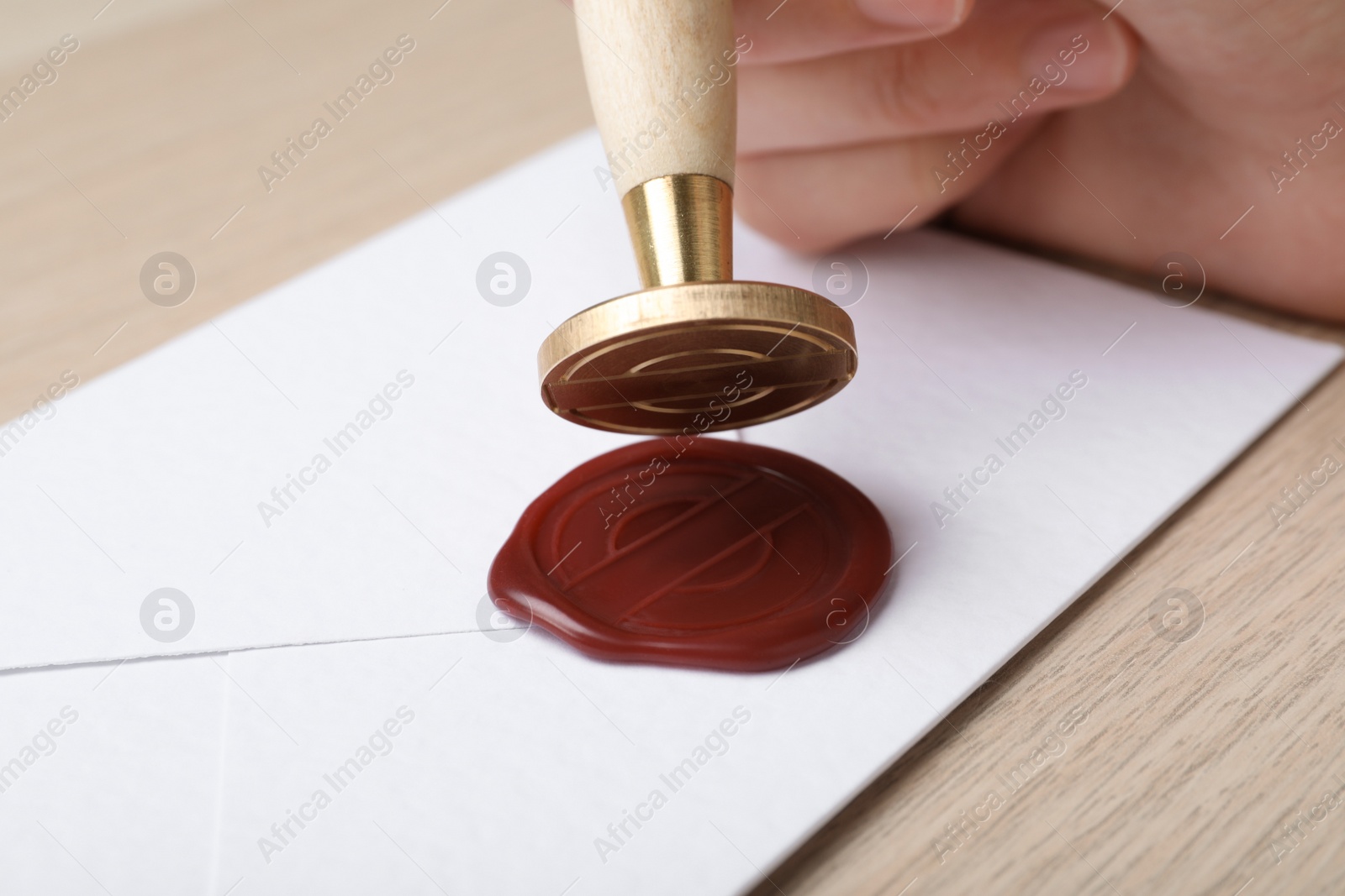 Photo of Woman sealing envelope at wooden table, closeup