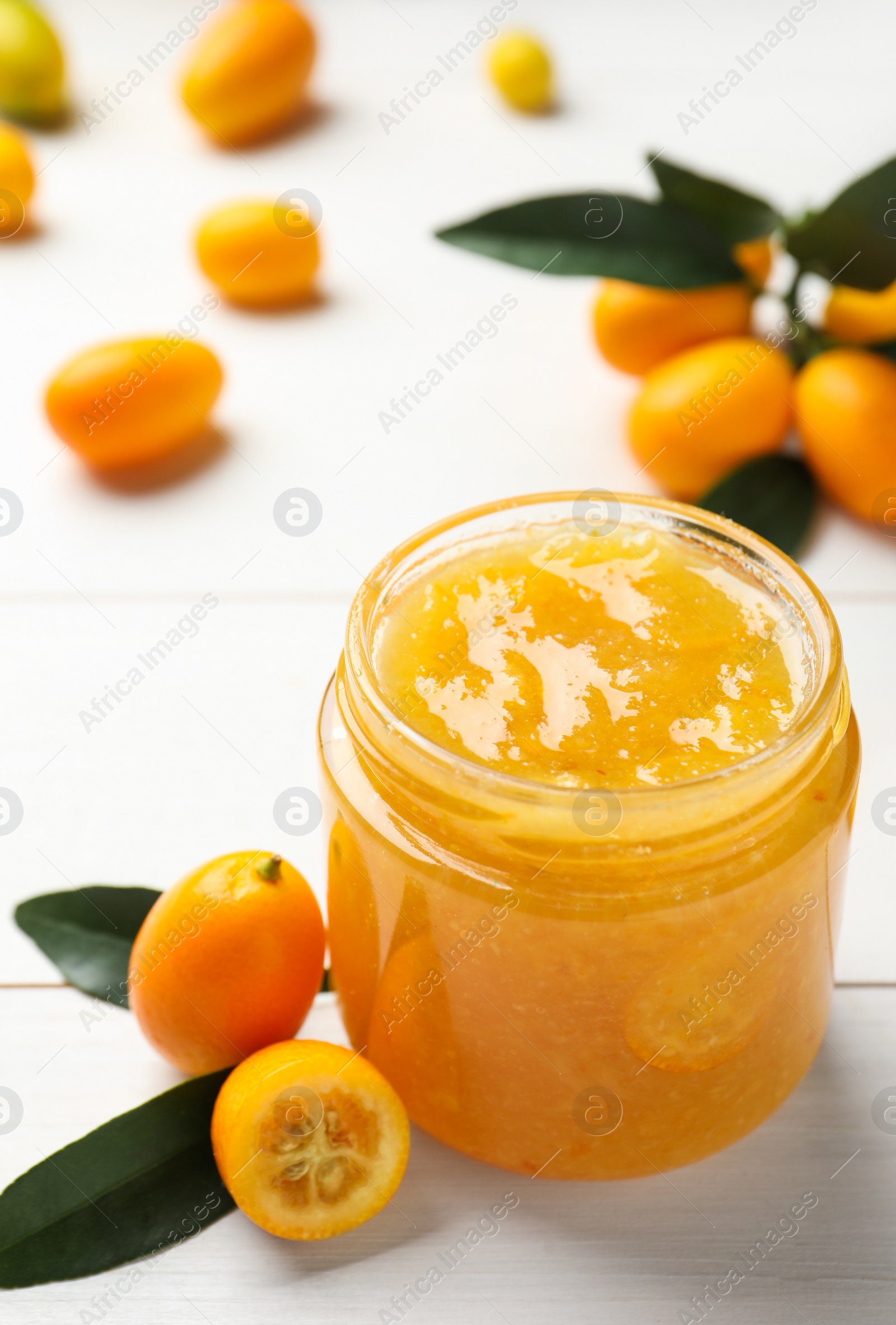 Photo of Delicious kumquat jam in jar and fresh fruits on white wooden table