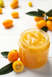 Delicious kumquat jam in jar and fresh fruits on white wooden table