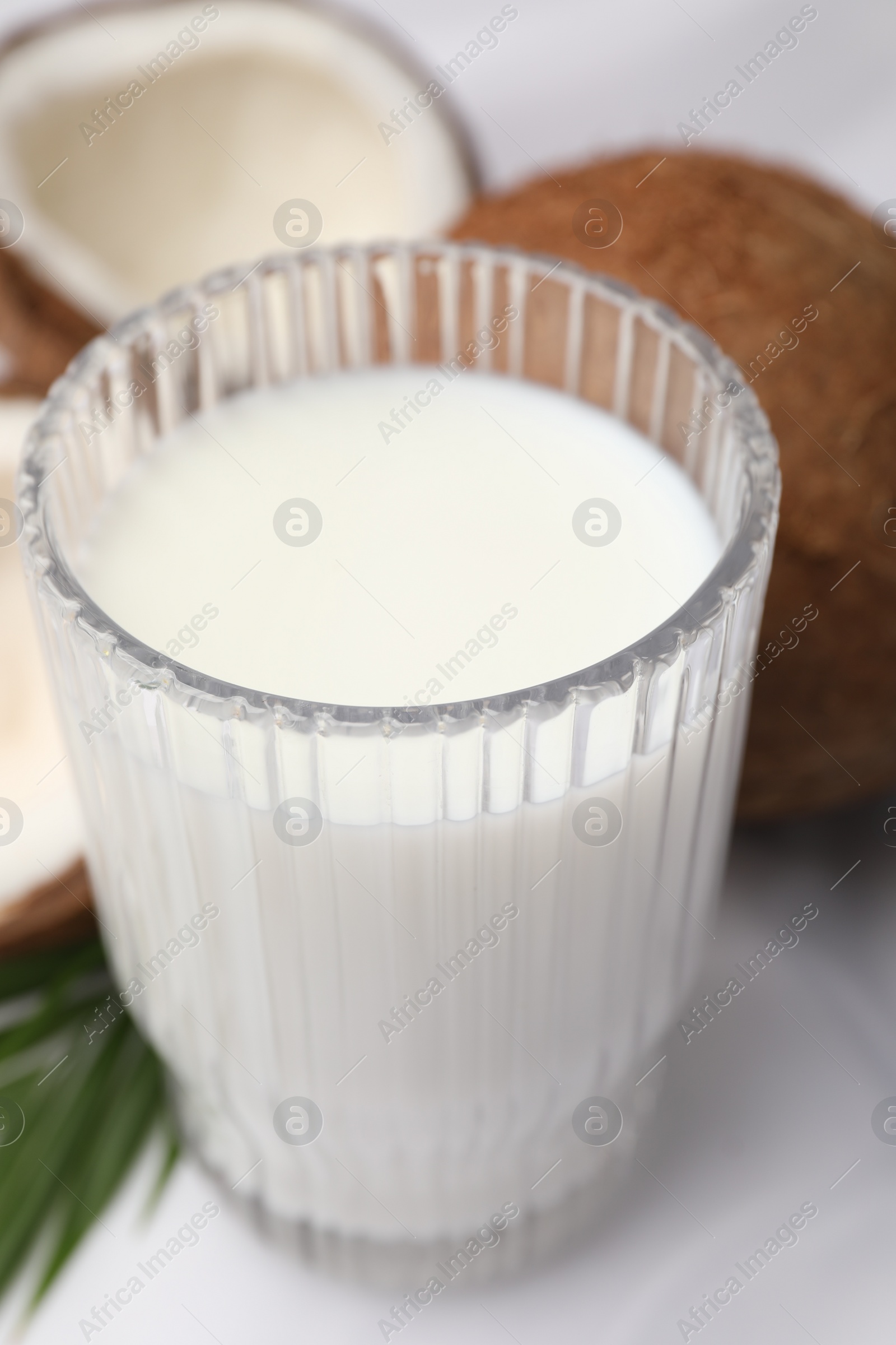 Photo of Glass of delicious coconut milk, palm leaf and coconuts on white table, closeup