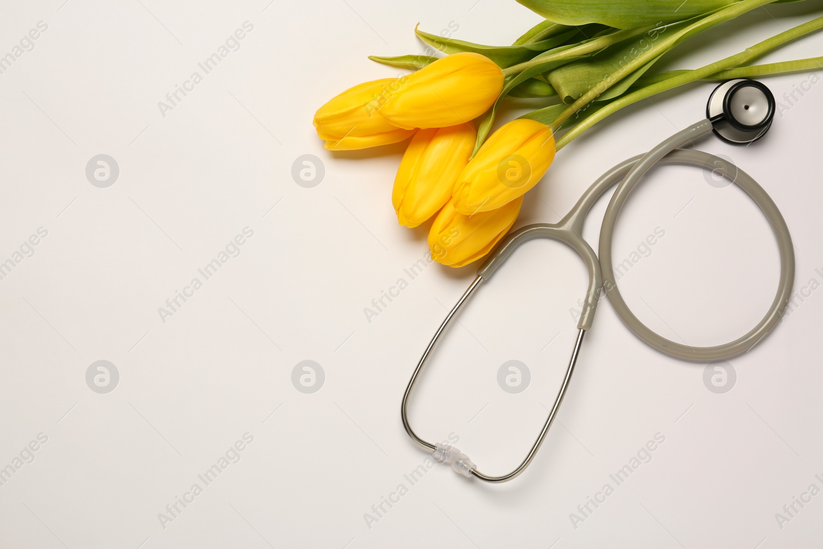 Photo of Stethoscope and yellow tulips on white background, flat lay with space for text. Happy Doctor's Day