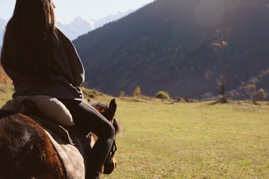 Photo of Back view of young woman riding horse in mountains on sunny day, space for text. Beautiful pet