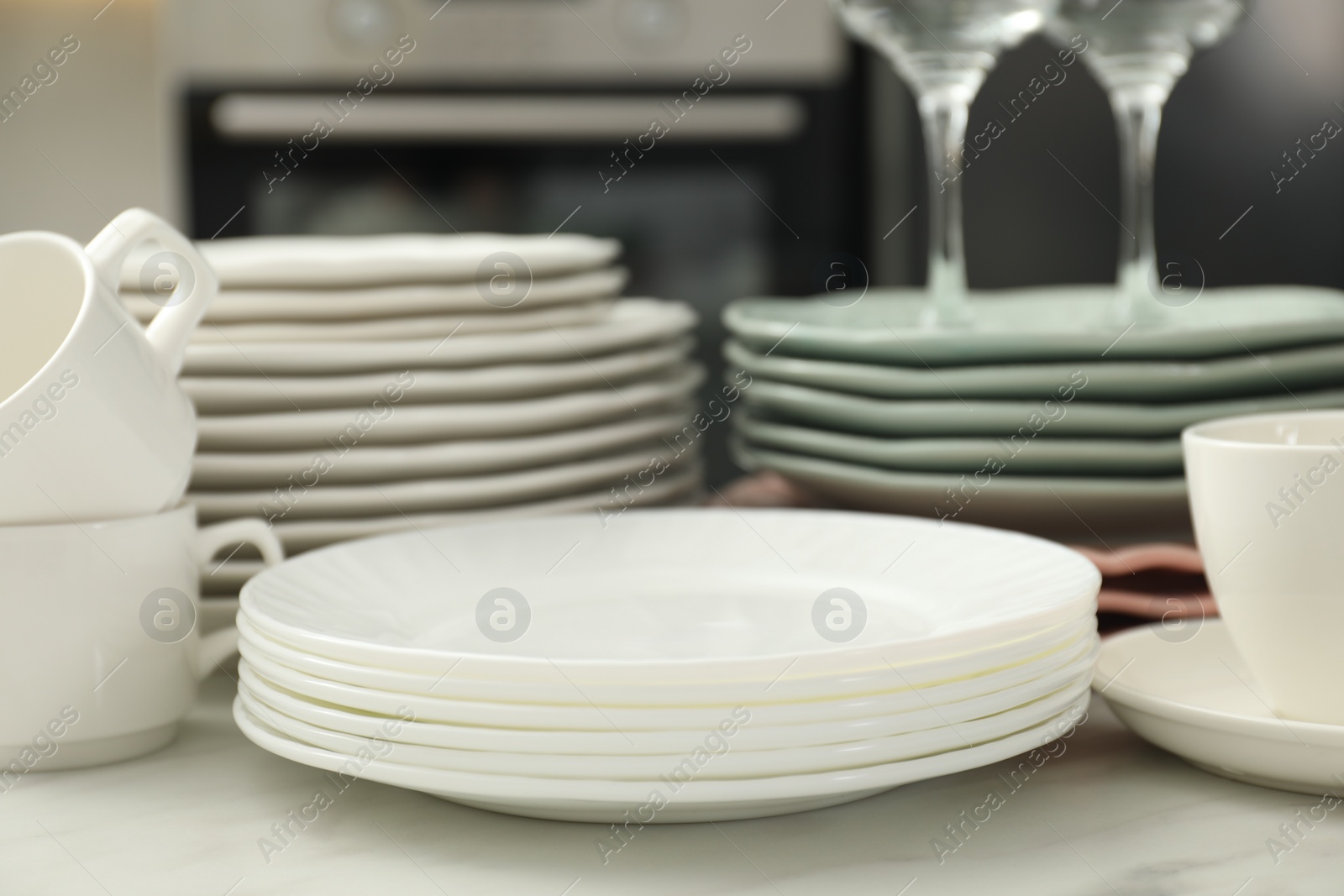 Photo of Clean plates and cups on white marble table in kitchen